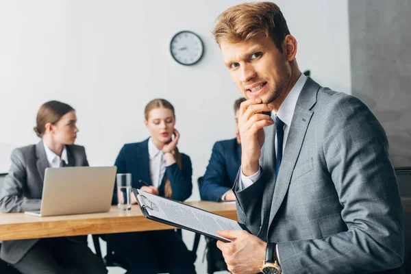 Selective focus of scared employee with resume looking at camera near recruiters in office — Stock Photo
