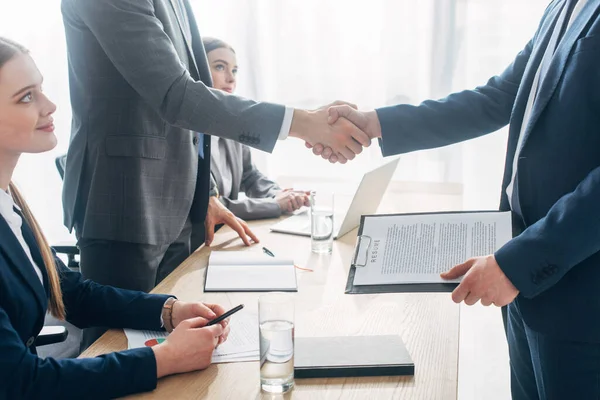 Side view of employee with resume shaking hands with recruiter during job interview in office — Stock Photo