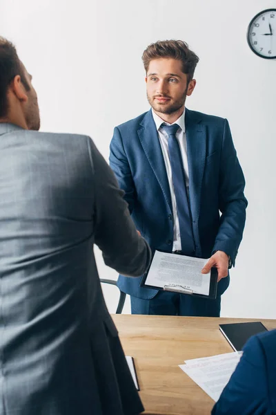 Selective focus of recruiter with clipboard shaking hands with employee in office — Stock Photo