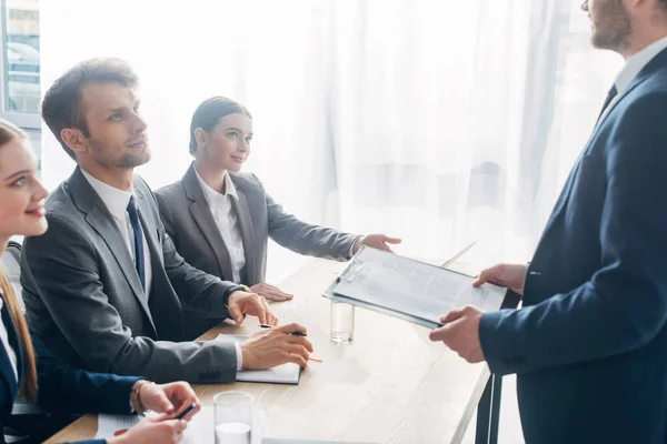 Side view of employee with clipboard standing near recruiters at table — Stock Photo