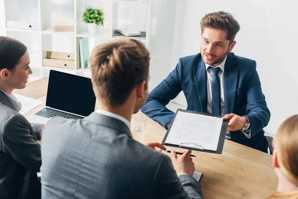 Selective focus of employee in formal wear holding resume near recruiters at table — Stock Photo