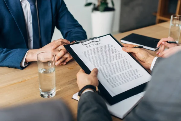 Cropped view of recruiter holding clipboard with resume near colleagues and employee — Stock Photo