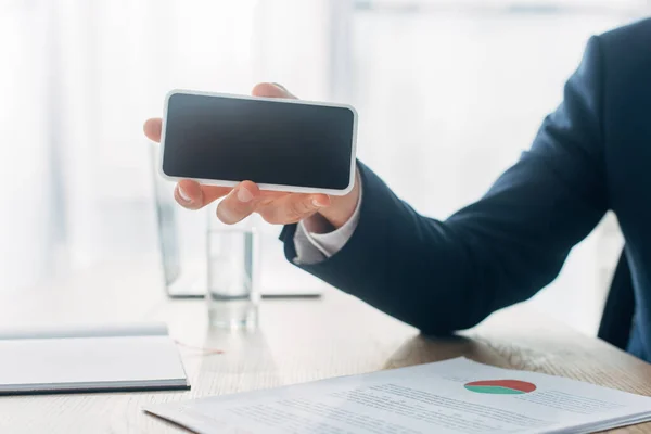 Cropped view of man holding smartphone with blank screen near papers with chart on table — Stock Photo