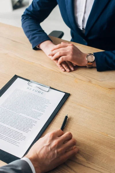 Cropped view of man holding pen near clipboard with resume and recruiter at table — Stock Photo