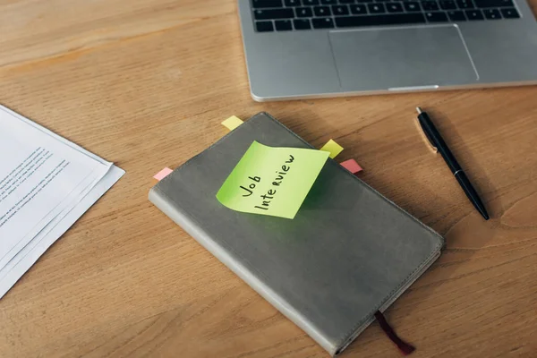 Notebook with job interview lettering on sticky note near laptop and documents on table — Stock Photo