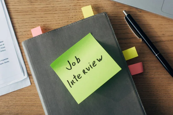 Top view of sticky note with job interview lettering near laptop and documents on wooden table — Stock Photo