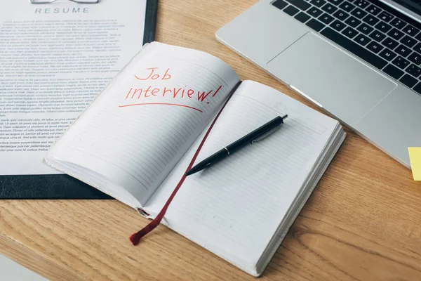 Escritura entrevista de trabajo en el cuaderno cerca de curriculum vitae y portátil en la mesa - foto de stock