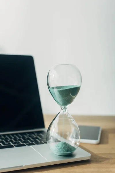 Vue rapprochée du sablier sur ordinateur portable près du smartphone sur la table dans le bureau — Photo de stock