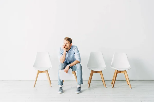 Handsome employee with hand near chin holding resume while sitting in office — Stock Photo