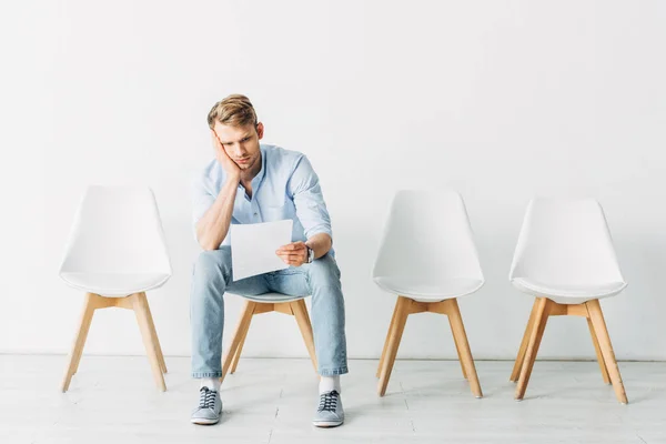 Hombre cansado mirando currículum mientras está sentado en la silla en la oficina - foto de stock