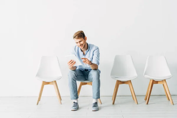 Funcionário sorrindo apontando com o dedo no tablet digital na cadeira no escritório — Fotografia de Stock