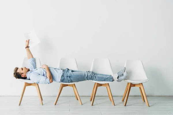 Side view of employee holding resume while lying on chairs in office — Stock Photo
