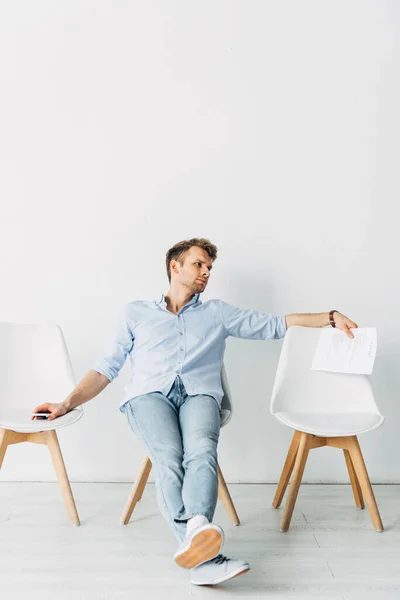 Empregado com currículo e smartphone olhando para longe na cadeira no escritório — Fotografia de Stock