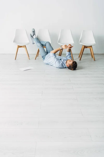 Vista de bajo ángulo del hombre usando el teléfono inteligente en el suelo mientras espera la entrevista de trabajo - foto de stock