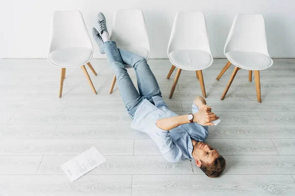 Vista ad alto angolo del dipendente che utilizza smartphone vicino al curriculum al piano — Foto stock