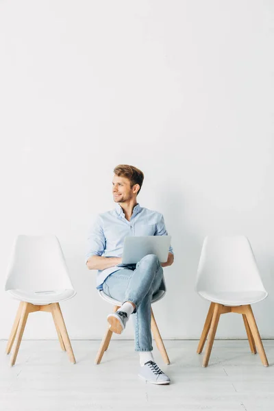 Empleado sonriente con portátil mirando hacia otro lado en la oficina - foto de stock