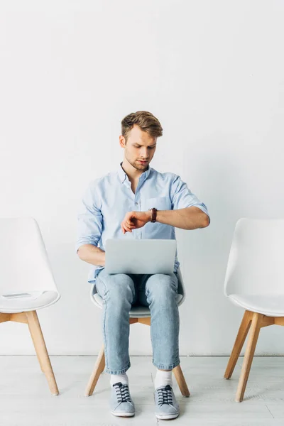 Employee with laptop looking at wristwatch in office — Stock Photo