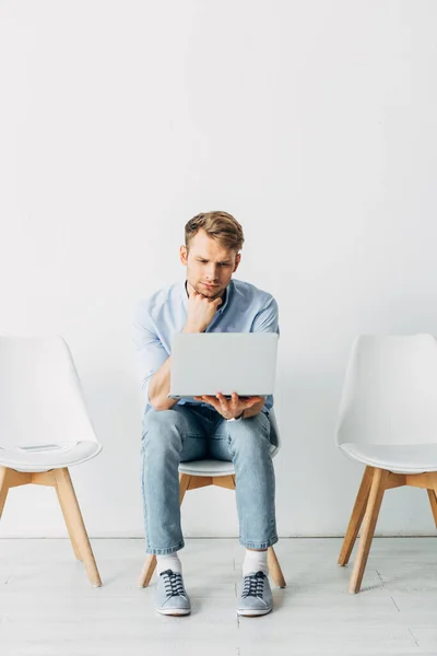 Man using laptop near smartphone and resume on chair in office — Stock Photo