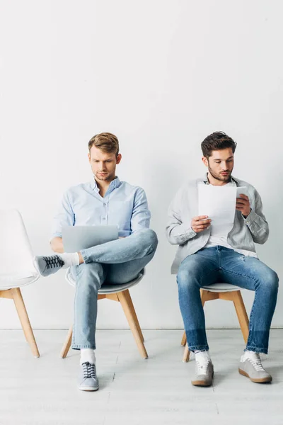 Empleado usando portátil cerca de hombre con curriculum vitae y teléfono inteligente en la oficina - foto de stock