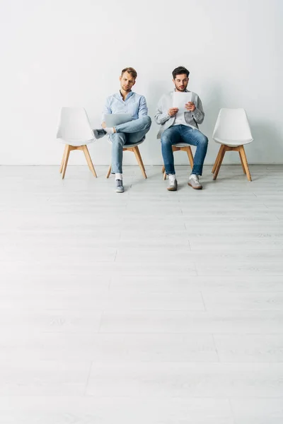 Schöne Angestellte mit Lebenslauf und Laptop sitzen auf Bürostühlen — Stockfoto