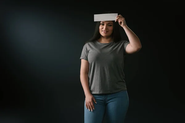 Vista frontal de plus size plus menina bonita com cartão epmty na testa em fundo preto — Fotografia de Stock