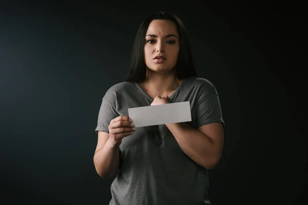 Front view of beautiful plus size girl confused and holding empty card on black background — Stock Photo