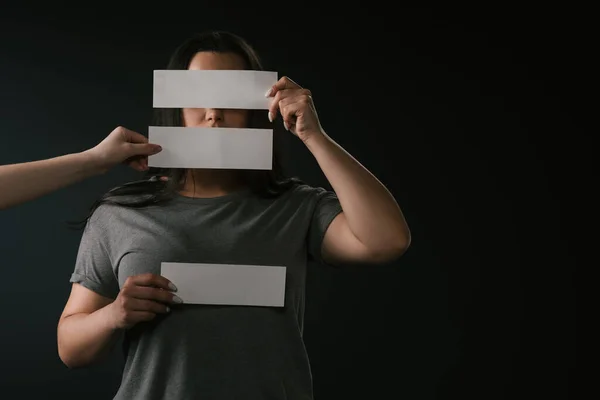 Vista frontal de la chica de tamaño grande cubriendo la cara bajo tarjetas vacías con espacio de copia sobre fondo negro - foto de stock