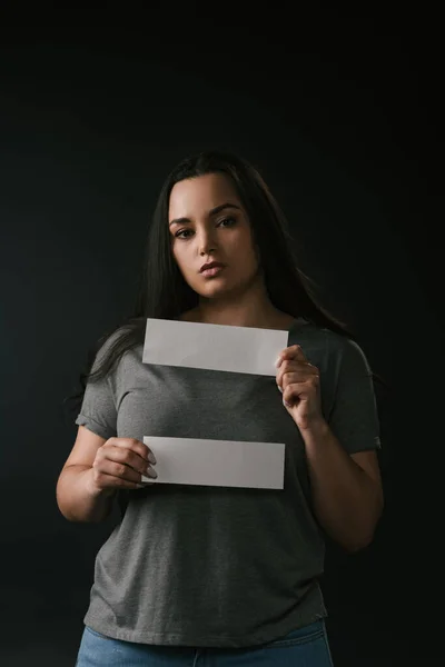 Vista frontal de chica de tamaño grande sosteniendo tarjetas vacías sobre fondo negro - foto de stock