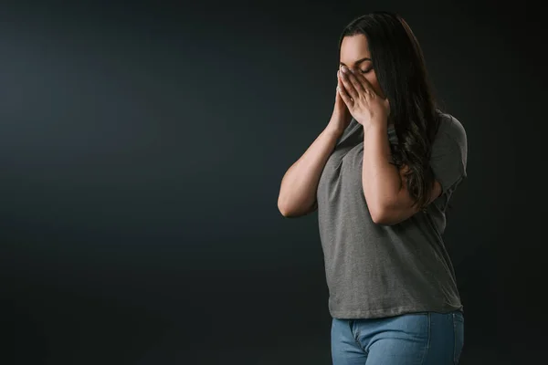 Triste plus size ragazza piangendo e coprendo il viso con le mani su sfondo nero — Foto stock