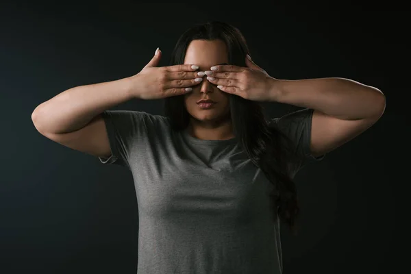 Front view of plus size girl performing blindness by covering eyes with hands on black background — Stock Photo