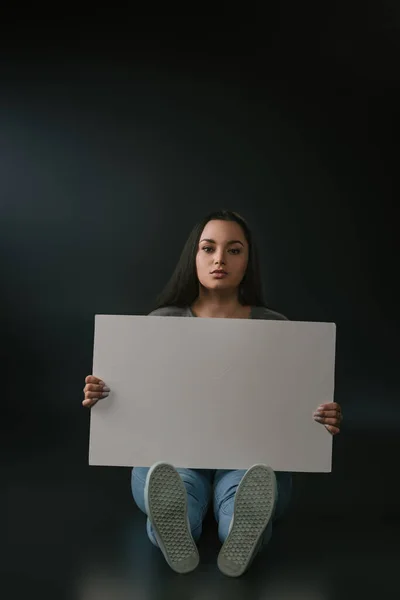 Front view of beautiful plus size girl sitting with empty board on black background — Stock Photo
