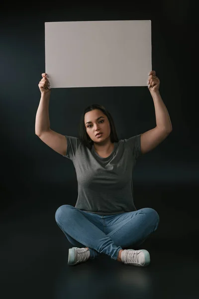 Vorderseite des Plus-Size-Girls demonstriert leeres Brett auf schwarzem Hintergrund — Stockfoto