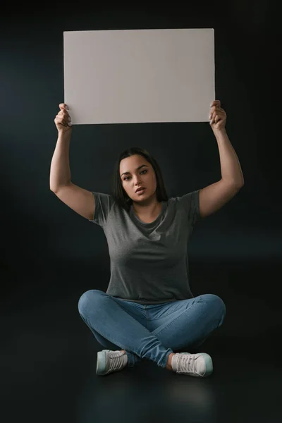 Vista frontal da menina plus size demostrando placa vazia no fundo preto — Fotografia de Stock