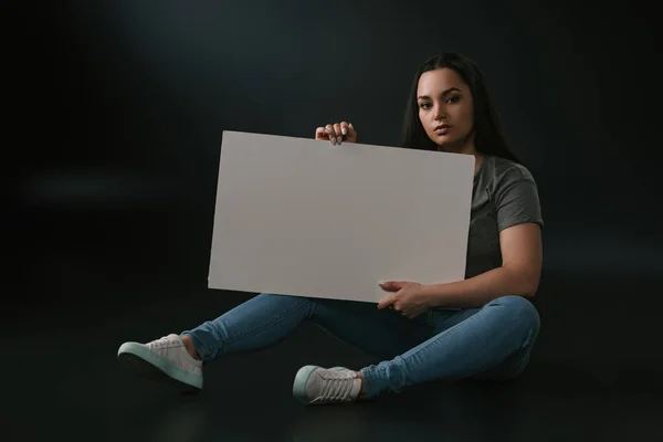 Vue de face de grave plus la taille fille assise avec planche vide sur fond noir — Photo de stock