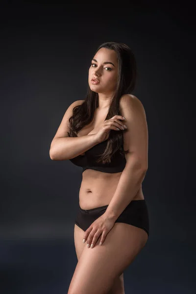 Plus Size Mädchen in Unterwäsche bedeckt Körper mit Händen auf schwarzem Hintergrund — Stockfoto