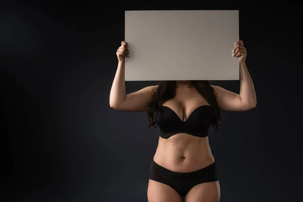 Front view of plus size model demonstrating empty board on black background — Stock Photo
