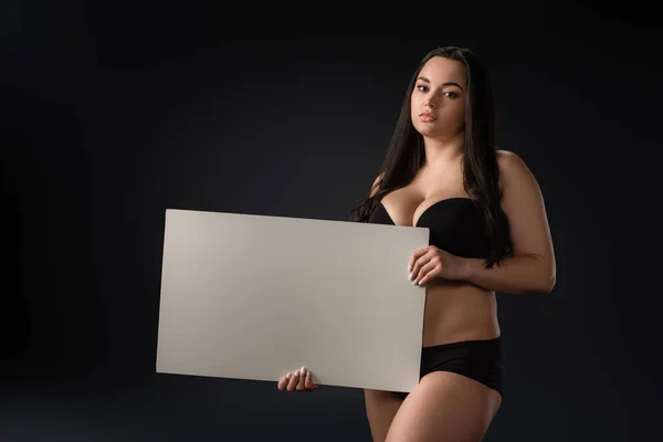 Beautiful plus size girl with empty board on black background — Stock Photo