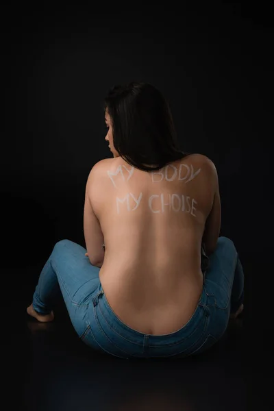Vista posteriore del modello plus size con scritte My Body My Choice sulla schiena nuda seduta su sfondo nero — Foto stock