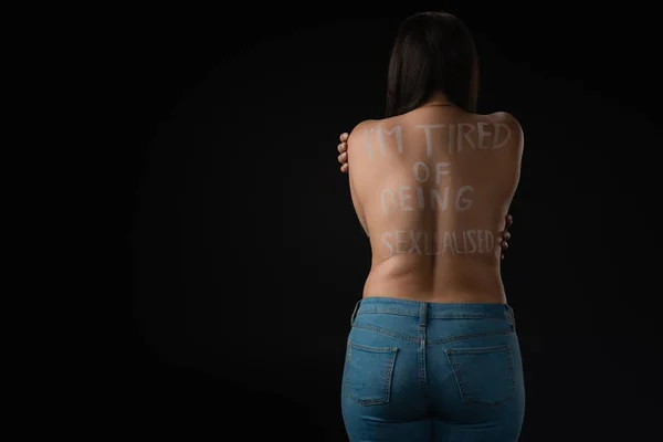 Rückenansicht des Plus-Size-Models, das ihren nackten Rücken mit Schriftzug umarmt I Am Tired of Being Sexualized isolated on black — Stockfoto