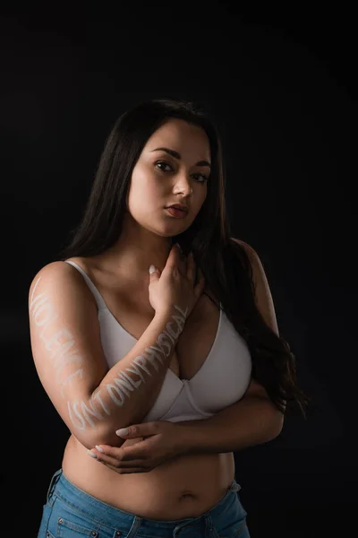 Half lenght view of plus size model in white bra with lettering Violence Is not Only Physical on hand isolated on black — Stock Photo