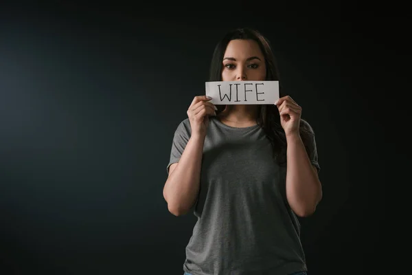 Front view of serious plus size girl holding card with word wife on black background — Stock Photo