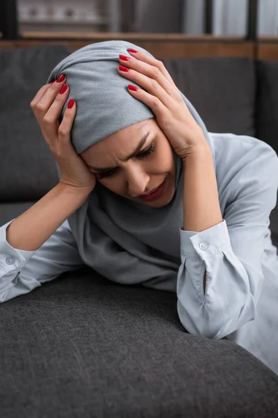Депрессивная мусульманка, трогающая хиджаб и плачущая в гостиной, концепция домашнего насилия — стоковое фото