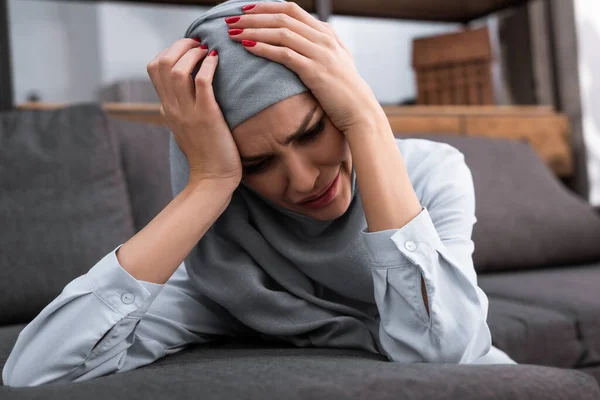 Mujer musulmana deprimida tocando hijab en la sala de estar, concepto de violencia doméstica - foto de stock