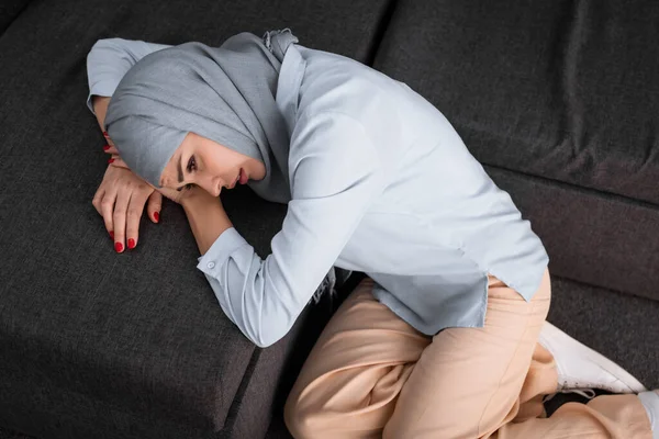 Visão aérea da mulher muçulmana deprimida no hijab deitada no sofá, conceito de violência doméstica — Fotografia de Stock