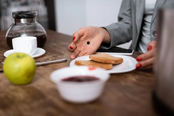 Selektiver Fokus der Frau mit schwarzem Punkt auf Palmteller mit Toastbrot in der Nähe von Apfel, Marmelade und Kaffeekanne, Konzept häuslicher Gewalt — Stockfoto