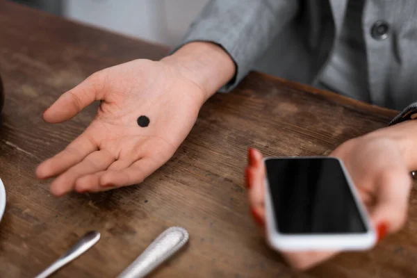 Vista ritagliata di donna con puntino nero sul palmo della mano smartphone con schermo bianco, concetto di violenza domestica — Foto stock