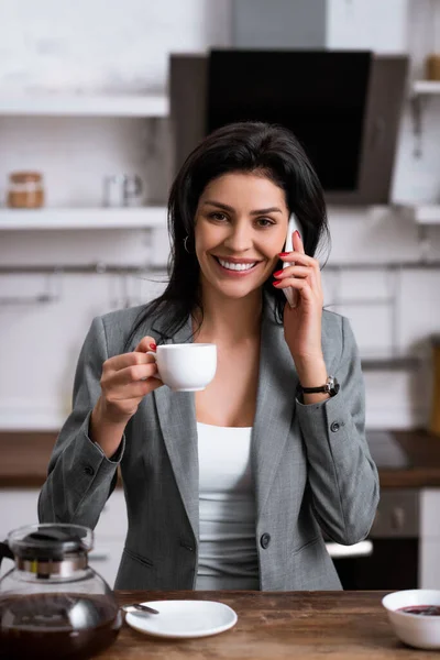 Donna d'affari sorridente che tiene una tazza di caffè e parla sullo smartphone mentre nasconde il problema della violenza domestica — Foto stock