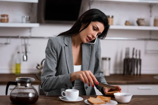 Attraktive Geschäftsfrau hält Messer in der Nähe von Toastbrot, während sie mit dem Smartphone spricht und das Problem häuslicher Gewalt versteckt — Stockfoto