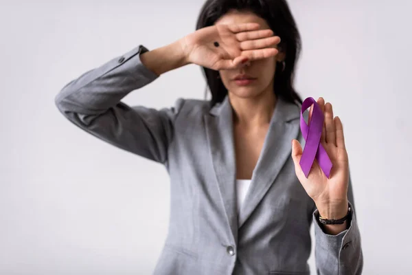 Selective focus of businesswoman with black dot on palm covering face and holding purple ribbon isolated on white, domestic violence concept — Stock Photo