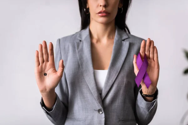 Cropped view of businesswoman with black dot on palm holding purple ribbon on white, domestic violence concept — Stock Photo